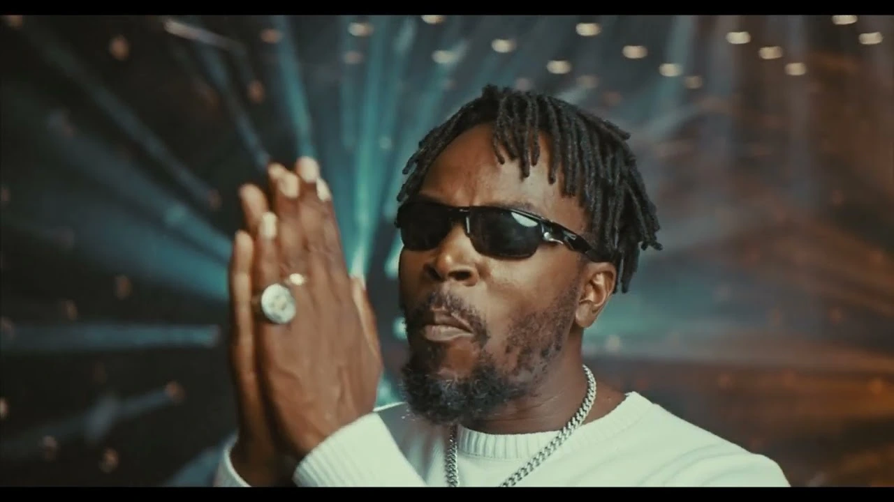 Thumbnail with the artiste doing a praying hands gesture. Song is "Kwaw Kese ft. Kofi Mole - Awoyo Sofo (Official Video)"